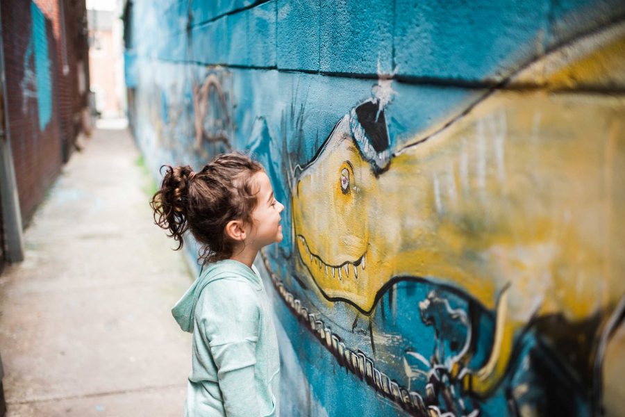 Little girl standing face to face with a painting of a dinosaur